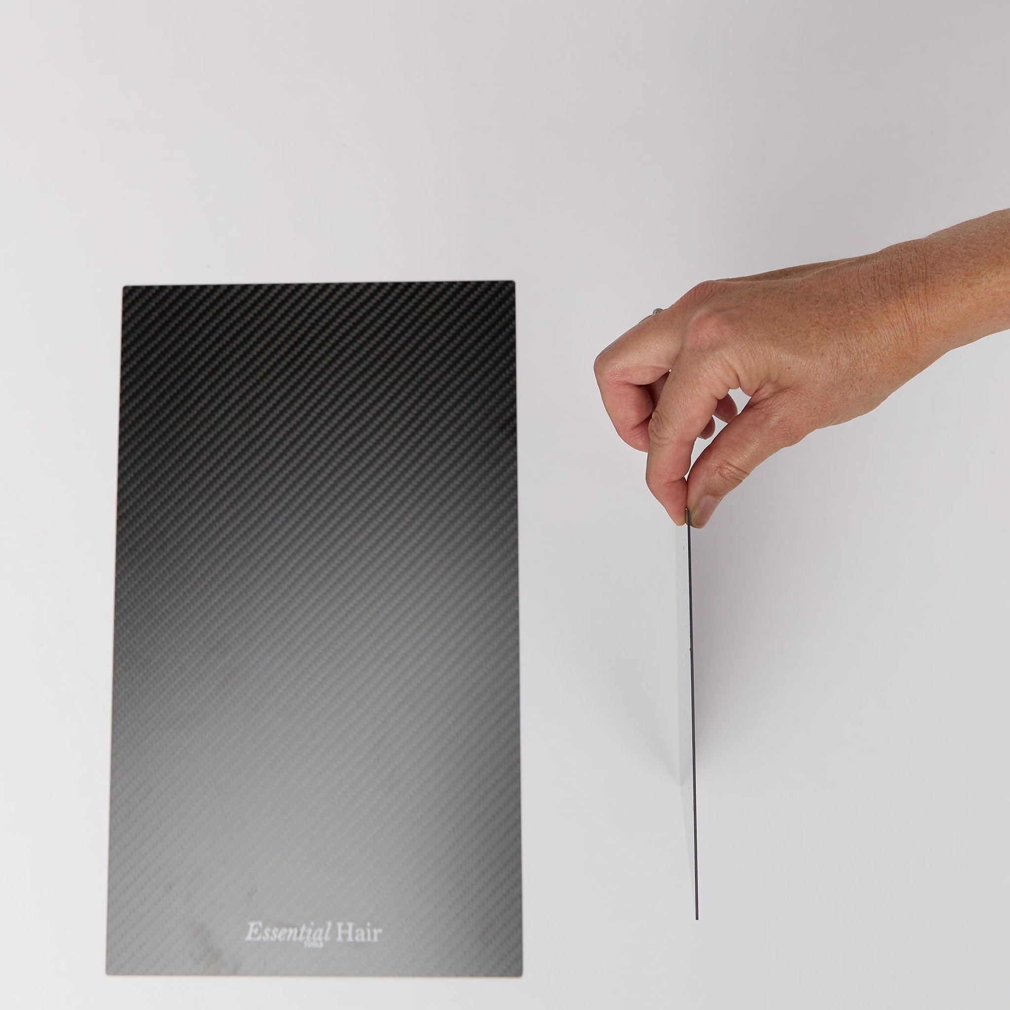 Hand holding the small carbon foil board edge-on to show its thin profile, next to the large board